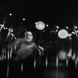 Maja Kasztelan fotograf - Czarno-białe zdjęcie pary obejmującej się na tle dekoracji świetlnych, widoczne odbicia w szklanej powierzchni.