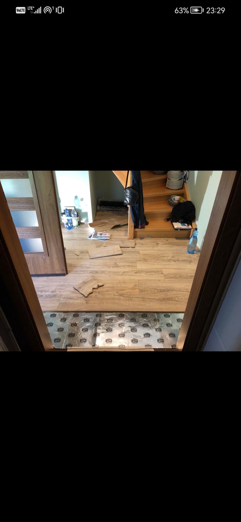 Układanie paneli podłogowych w przedpokoju z widoczną izolacją akustyczną, fragmentem schodów i drzwiami z przeszkleniami.