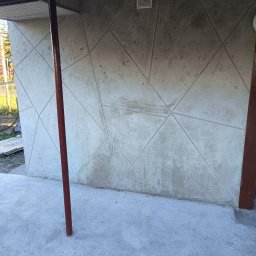 W.R. REMONTY WALDEMAR RATAJCZAK - Ściana budynku z dekoracyjną, geometryczną fakturą w odcieniach szarości, widoczna część podłogi i fragment osoby w tle.