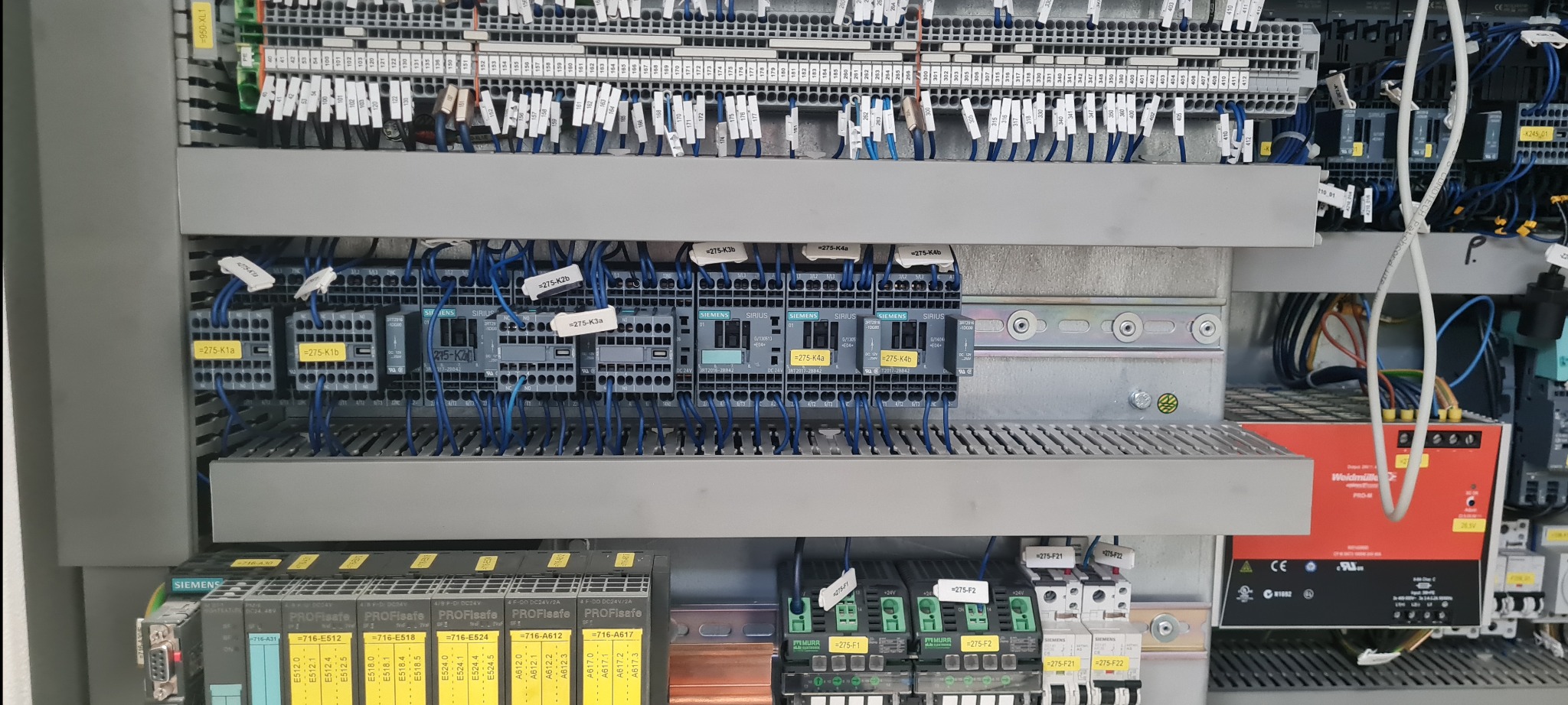 Rozdzielnica elektryczna z widocznymi modułami sterującymi Siemens Sirius, okablowaniem i oznaczeniami, zamontowana w szarej obudowie.