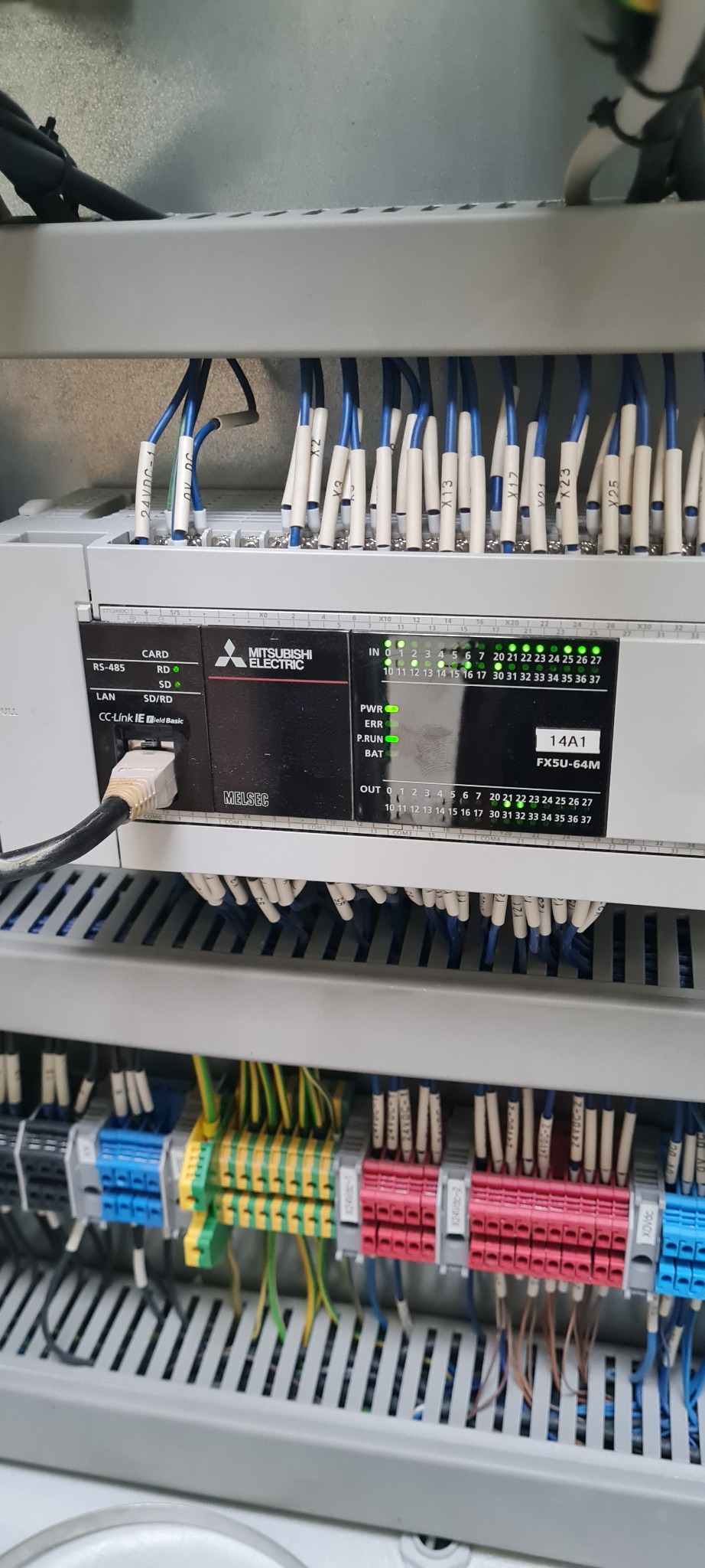 Panel sterowania Mitsubishi Electric MELSEC FX5U-64M z podłączonymi przewodami oznaczonymi etykietami, widoczne diody sygnalizacyjne i złącza.