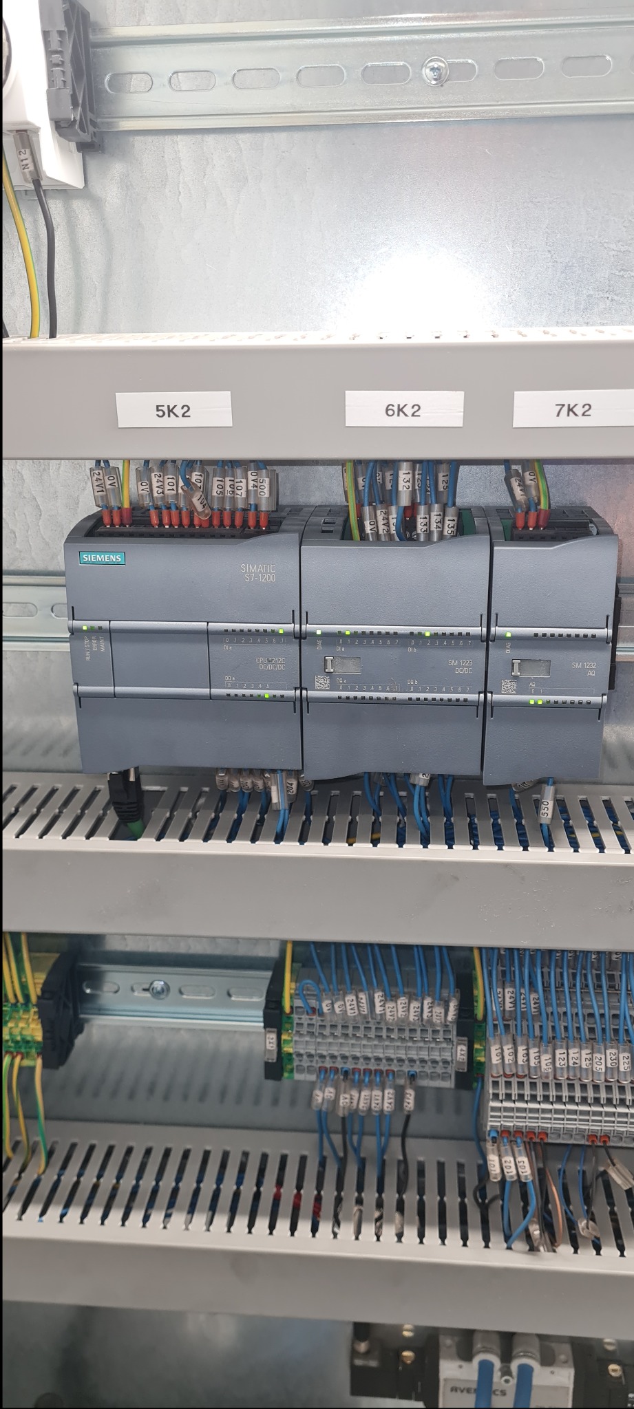 Panel sterowania z trzema modułami Siemens Simatic S7-1200, oznaczonymi etykietami 5K2, 6K2 i 7K2, z podłączonymi przewodami oznaczonymi numerami, zamontowany w metalowej szafie elektrycznej.