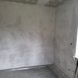 ANDROBUD - Wnętrze pokoju w trakcie prac wykończeniowych: szpachlowane ściany, fragment sufitu z płyt karton-gips, metalowy profil przy podłodze. Widoczne ślady po otworach.