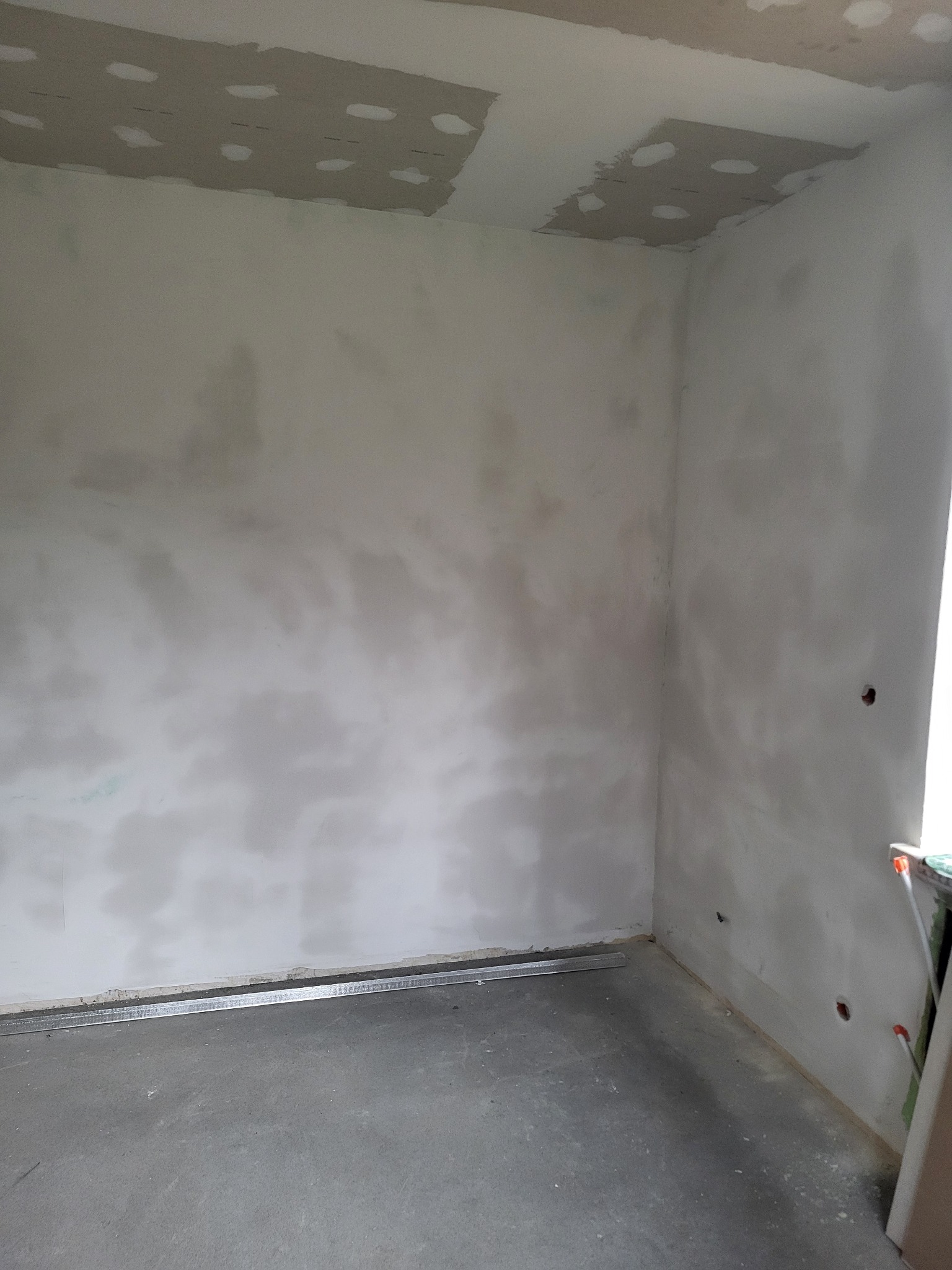 Wnętrze pokoju w trakcie prac wykończeniowych: szpachlowane ściany, fragment sufitu z płyt karton-gips, metalowy profil przy podłodze. Widoczne ślady po otworach.