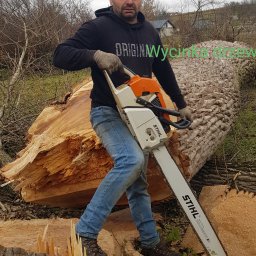 Anna Patro Domikop - Mężczyzna w czapce i bluzie z napisem 'ORIGINAL' pozuje z piłą spalinową Stihl na tle ściętego pnia drzewa z widocznymi śladami cięcia.