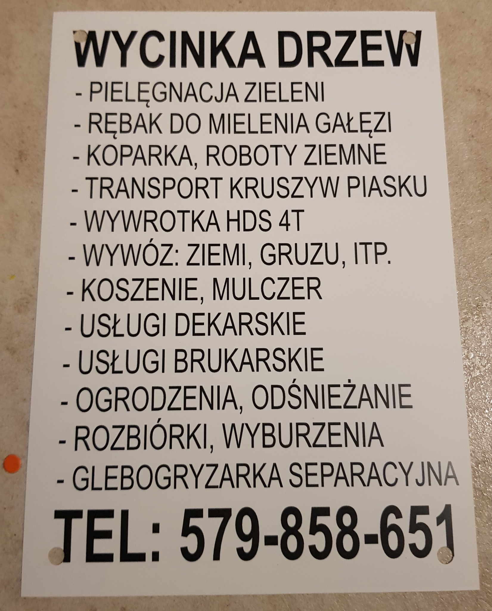 Tablica informacyjna z ofertą usług: wycinka drzew, pielęgnacja zieleni, rębakiem do mielenia gałęzi, koparką, robót ziemnych, transport kruszyw piasku, wywrotka HDS 4T, wywóz ziemi, gruzu...