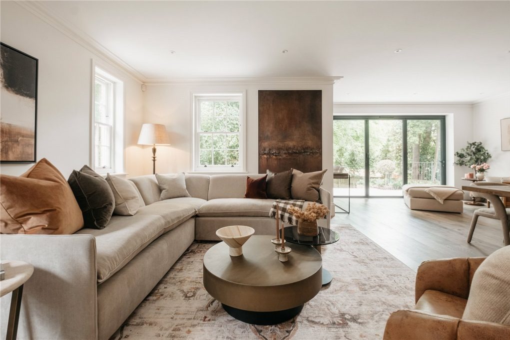 Jasny salon z narożną sofą, okrągłym stolikiem kawowym i dużym obrazem na ścianie, widok na ogród przez przesuwne drzwi balkonowe.