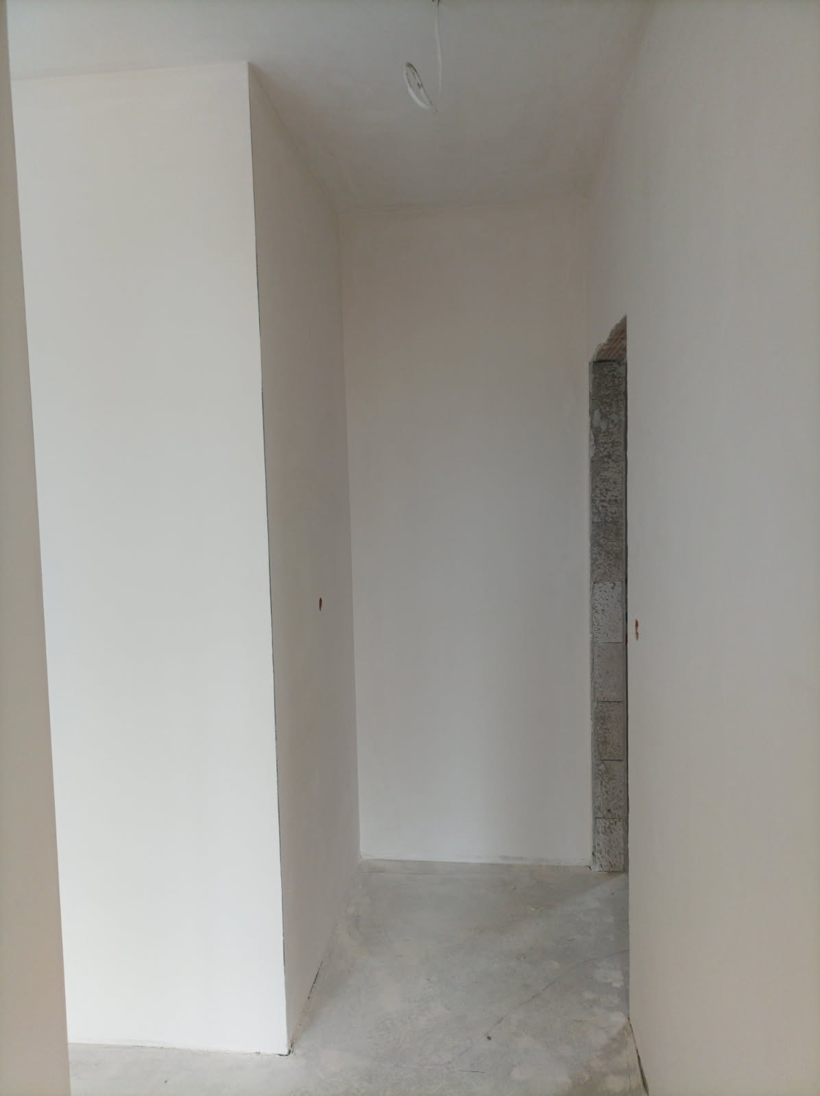 Korytarz po gładziowaniu ścian, widoczne ślady po szpachlowaniu na podłodze i surowa ościeżnica drzwiowa.