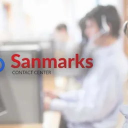 Uśmiechnięta blondynka w słuchawkach, pracująca w biurze, z logo firmy na ekranie monitora.