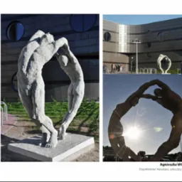 Kompozycja z dwóch rzeźb z jasnego kamienia, przedstawiających postacie w dynamicznej pozie, na tle nowoczesnego budynku z okrągłymi oknami i fragmentu parkingu w słoneczny dzień.