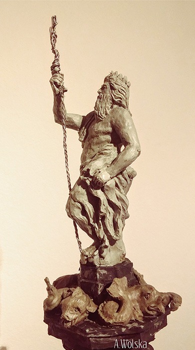 Gliniasta statuetka Posejdona z trójzębem, na cokole z motywami morskimi, w ciepłej tonacji. Widoczny podpis autora: A. Wolska.