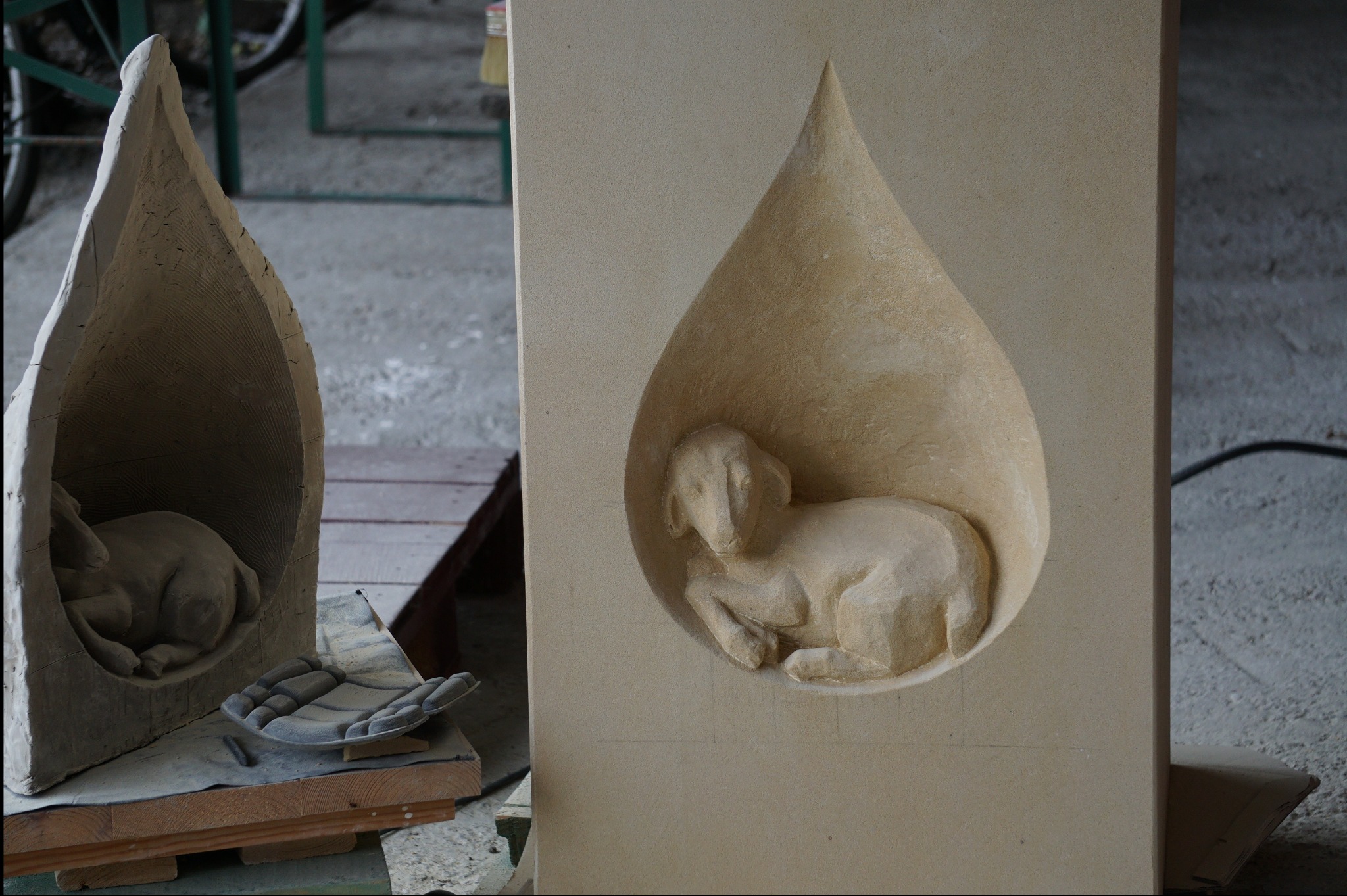 Ręcznie rzeźbiony w piaskowcu motyw baranka w kształcie łzy, obok druga rzeźba w surowym wykończeniu, dłuta kamieniarskie. Detal pracy kamieniarskiej.