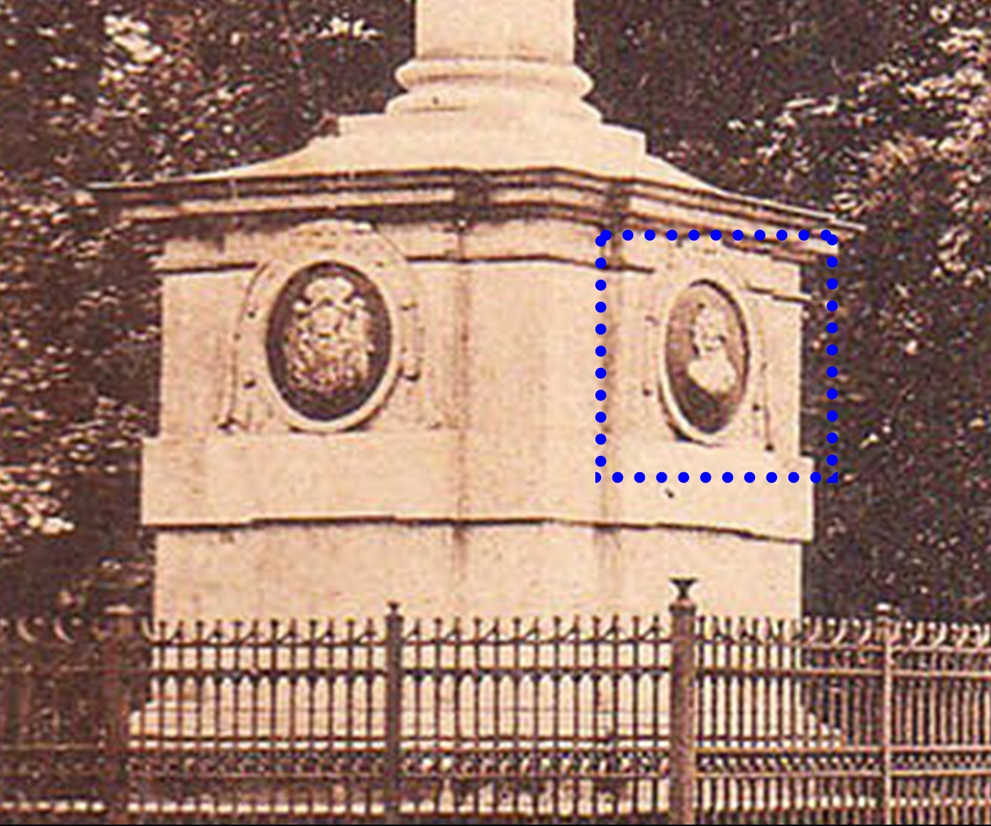 Sepiowy pomnik z płaskorzeźbami portretowymi i herbem, ogrodzony żeliwnym płotem. Widoczne detale architektoniczne i faktura kamienia. Stare zdjęcie.