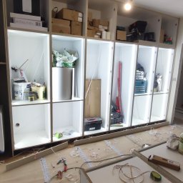 Mikalai Voitau - Montaż szafy wnękowej z oświetleniem LED. Widoczne narzędzia i akcesoria montażowe. Szafa w trakcie instalacji, z otwartymi półkami i elementami wyposażenia.