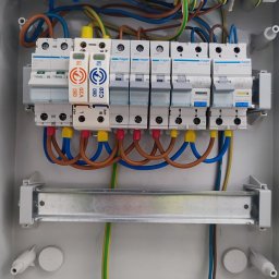 Mikalai Voitau - Rozdzielnica elektryczna Hager z zainstalowanymi bezpiecznikami i przewodami o różnych kolorach, zamontowana w szarej obudowie. Widoczne elementy instalacji elektrycznej.