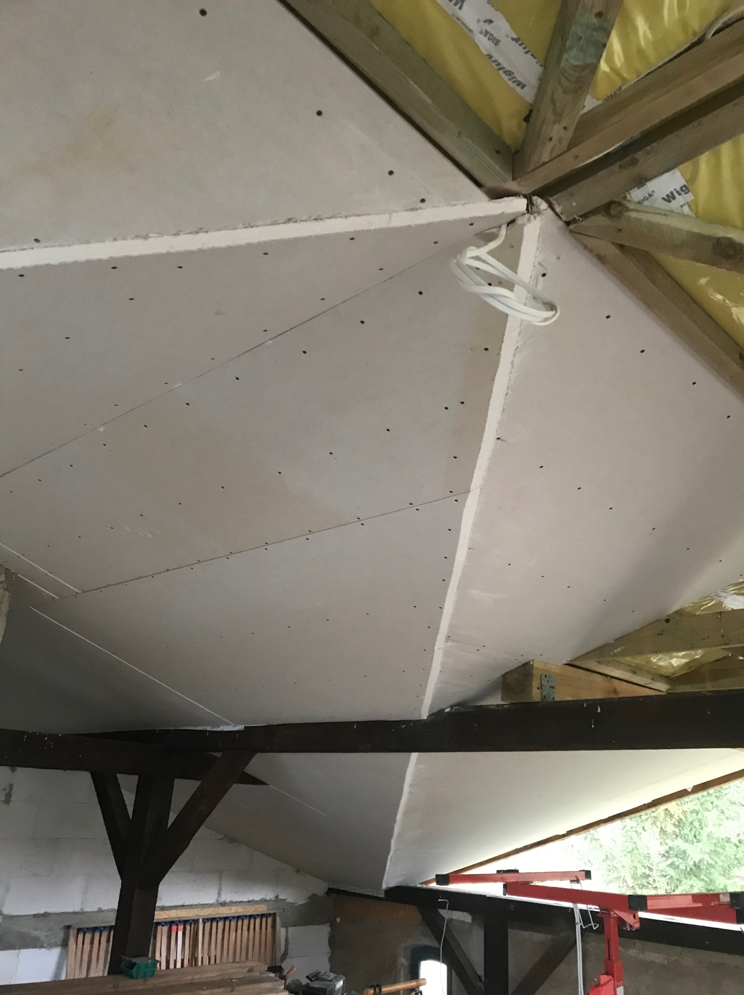 Montaż płyt karton gips na skośnym suficie poddasza w Ostromicach, widoczne drewniane elementy konstrukcyjne dachu i wiszące przewody elektryczne.