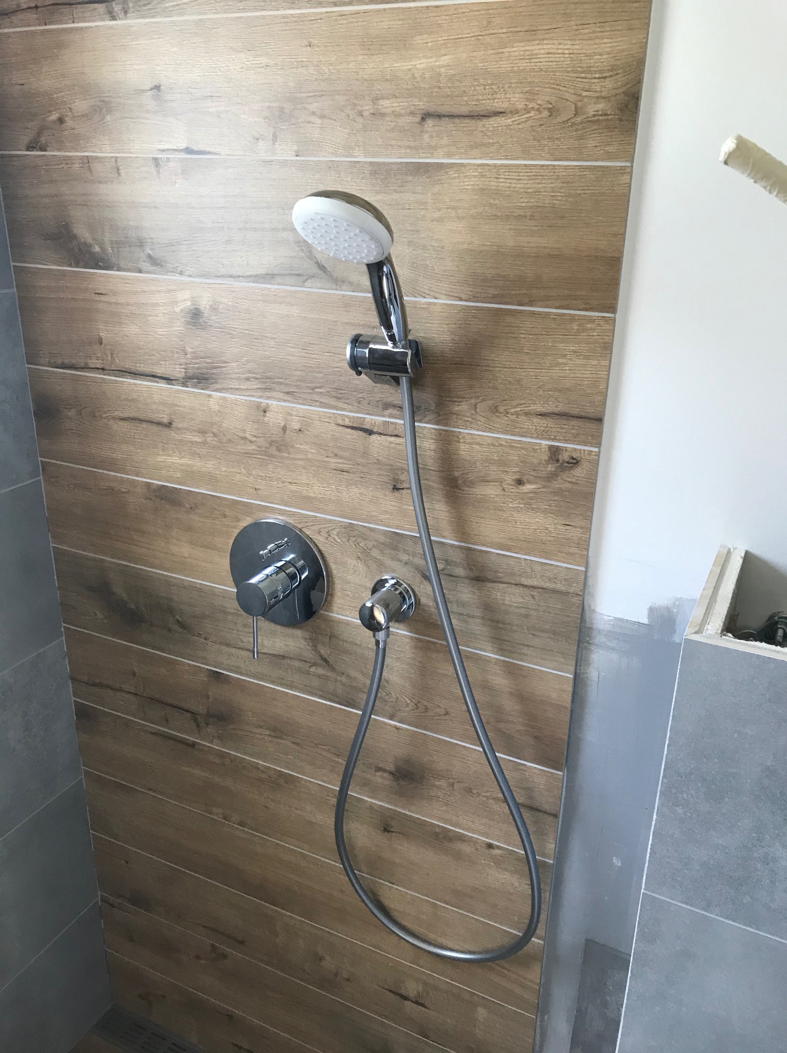 Nowoczesna kabina prysznicowa z baterią podtynkową i deszczownicą, ściany wyłożone płytkami imitującymi drewno, widoczne ślady po malowaniu na ścianie