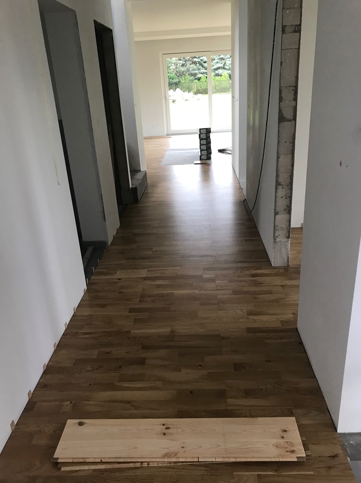 Korytarz w trakcie układania parkietu, widoczne deski parkietu na podłodze, listwy dystansowe przy ścianie i surowa ściana z cegieł