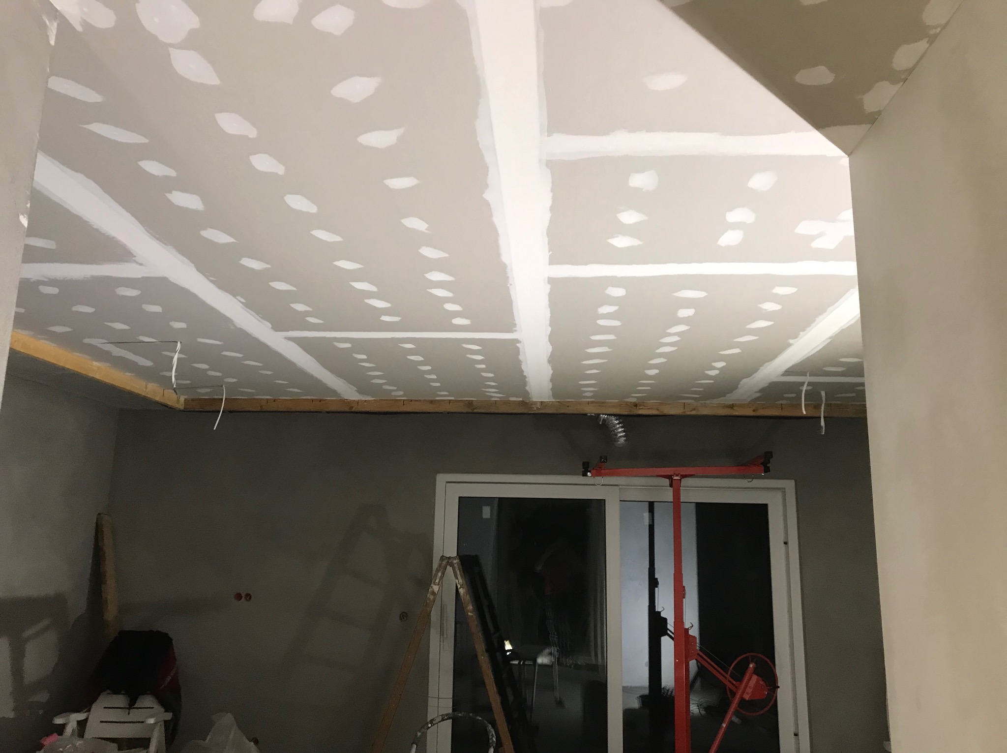 Sufit z płyt kartonowo-gipsowych w trakcie szpachlowania, widoczne łączenia płyt i wkręty, na podłodze drabina i podnośnik do płyt.