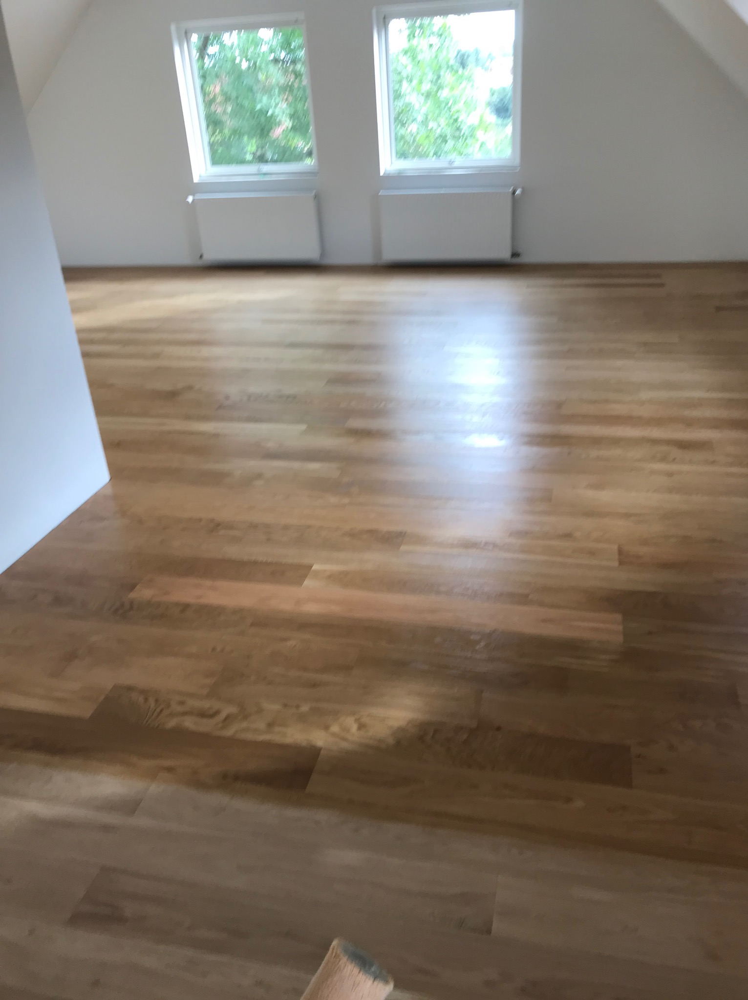 Jasny, nowo ułożony parkiet w pokoju na poddaszu z dwoma oknami dachowymi i białymi grzejnikami.