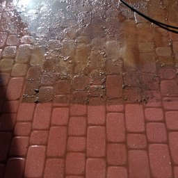 Lavador Łukasz Biazik - Częściowo umyta, mokra kostka brukowa w odcieniach czerwieni, z widocznym kontrastem między czystą a brudną powierzchnią.