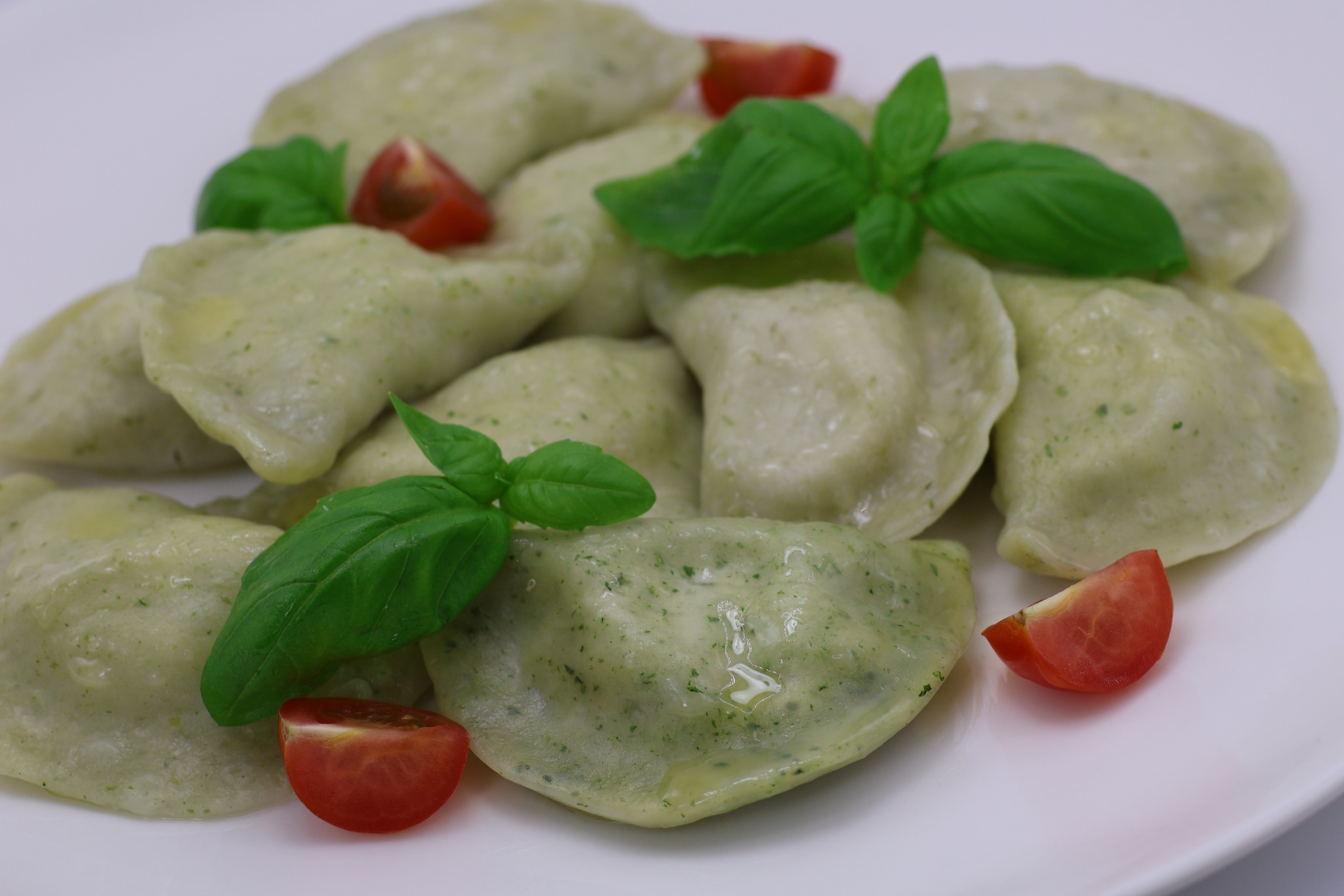 Porcja pierogów z zielonym nadzieniem, udekorowana listkami bazylii i ćwiartkami pomidora, podana na białym talerzu.