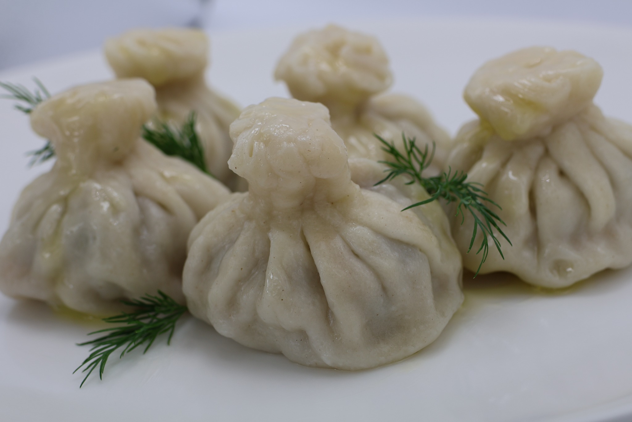 Pięć gruzińskich pierogów chinkali na białym talerzu, udekorowanych gałązkami świeżego koperku.