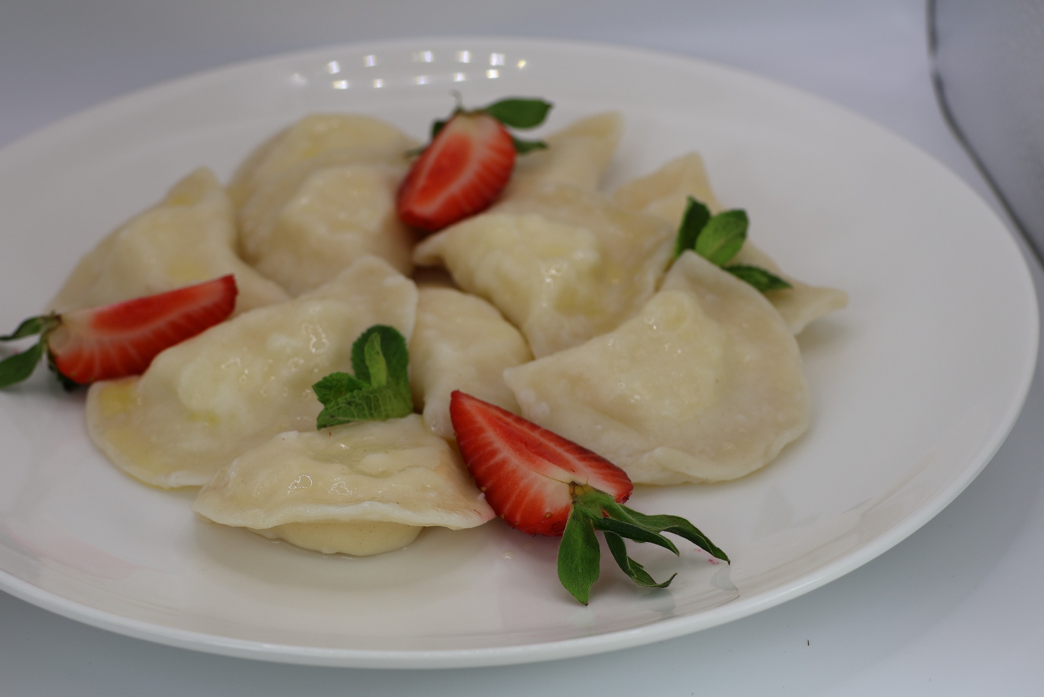 Porcja pierogów z serem, udekorowana świeżymi truskawkami i listkami mięty na białym talerzu.