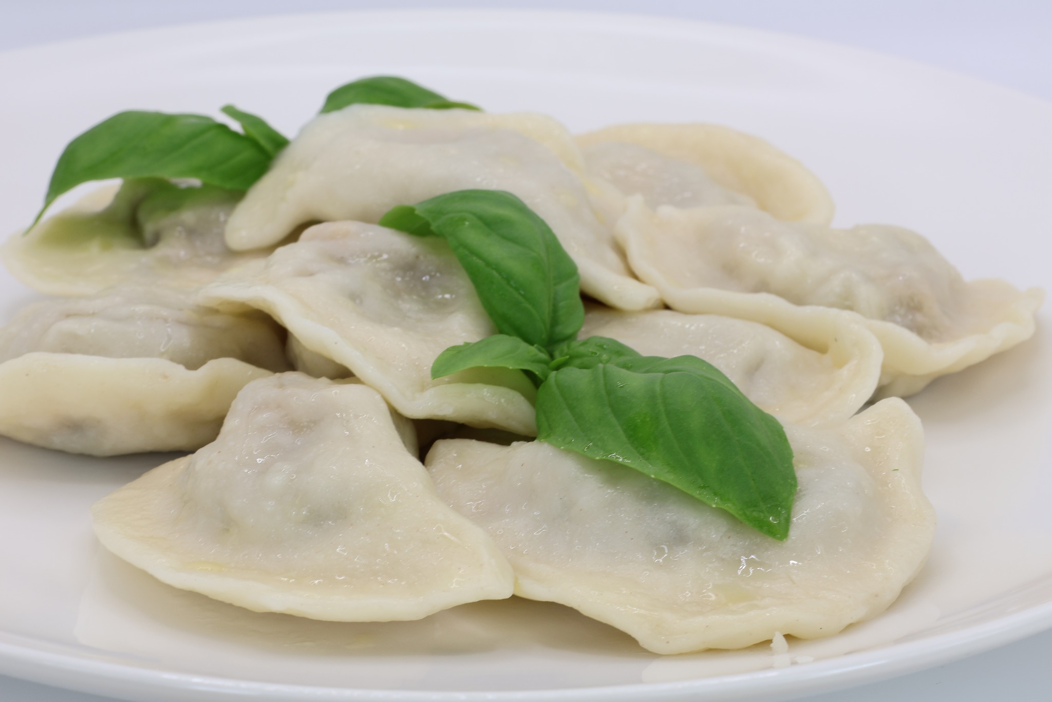 Porcja świeżych, gotowanych pierogów z mięsem, udekorowanych listkami bazylii, na białym talerzu, serwowana przez firmę cateringową ze Szczecina.