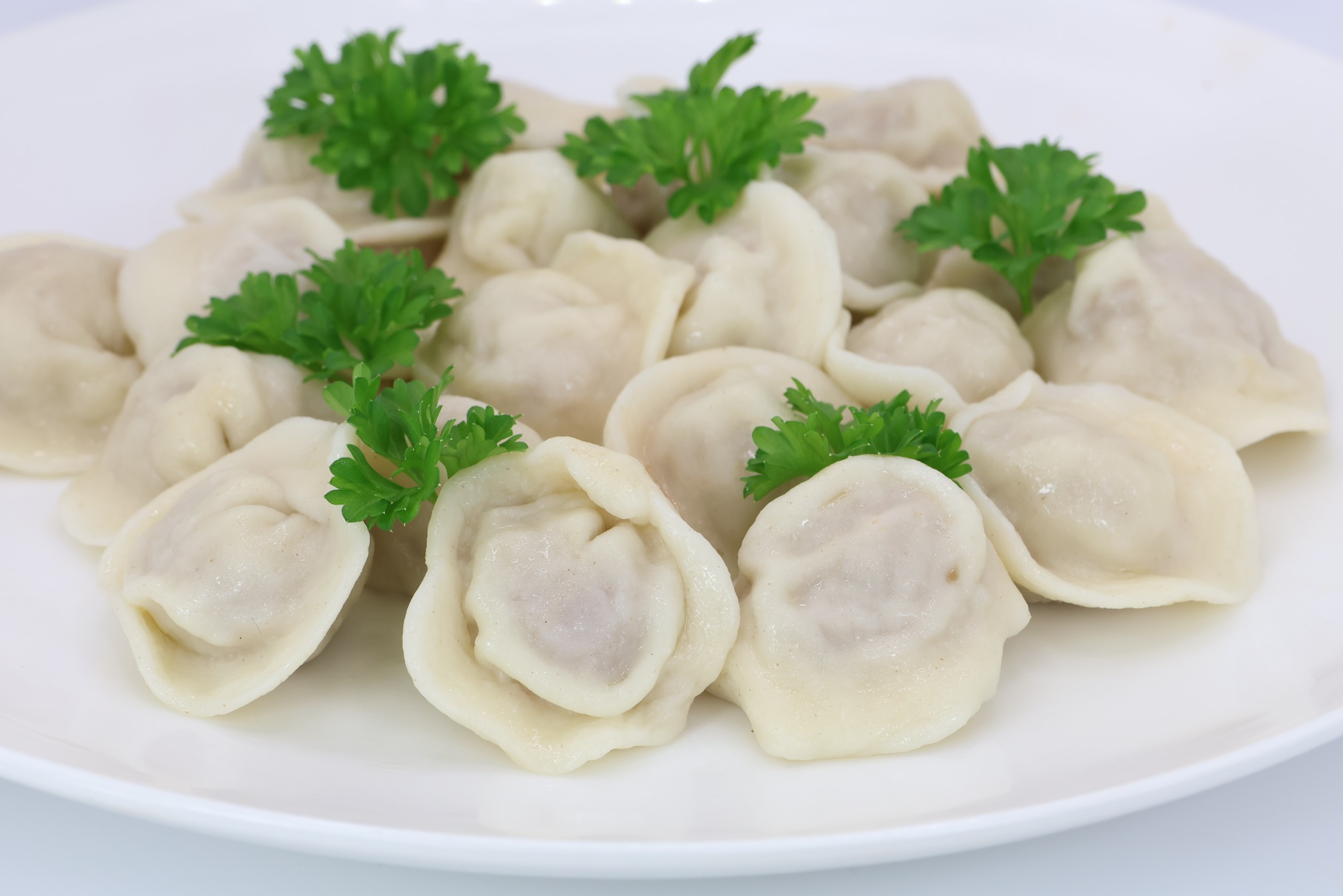 Ułożone na białym talerzu pierogi z mięsem, udekorowane świeżą zieloną pietruszką.