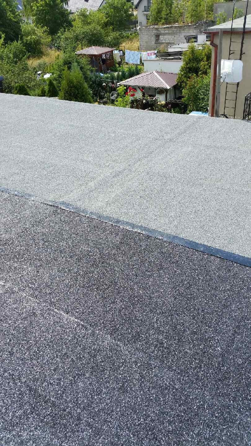 Dach pokryty papą termozgrzewalną z widocznym łączeniem dwóch warstw o różnej kolorystyce, na tle zabudowań i zieleni.