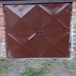 KołekSpaw - Dwuskrzydłowa brama garażowa w kolorze brązowym z geometrycznym wzorem rombów, zamykana na zasuwkę, umieszczona w murze z czerwonej cegły, widoczna z zewnątrz na tle zieleni drzew.