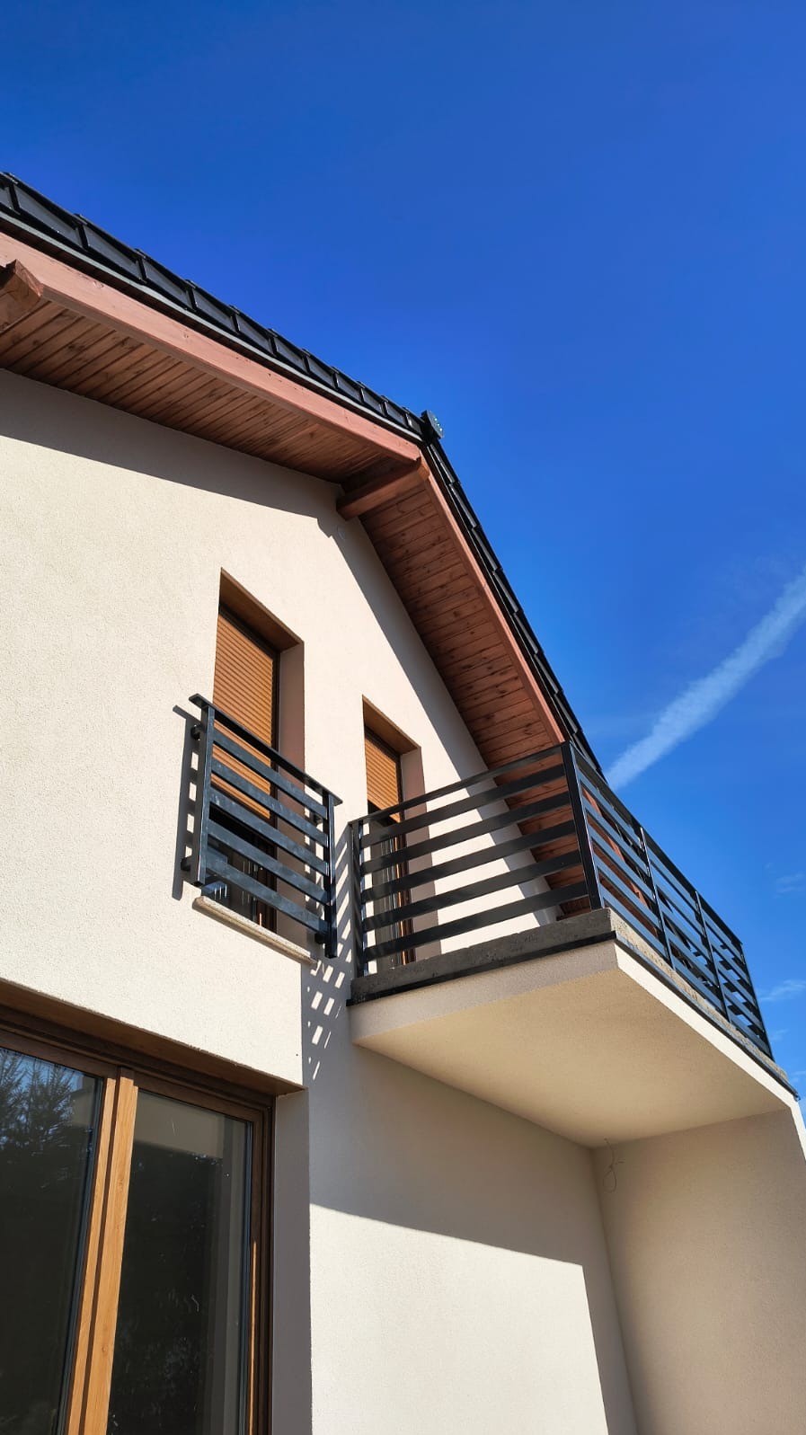 Nowoczesna, czarna balustrada balkonowa z poziomych profili na tle błękitnego nieba. Ujęcie z dołu, eksponujące geometrię i minimalistyczny design.