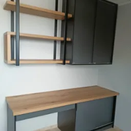 Nowoczesny zestaw mebli: biurko z drewnianym blatem i szarą podstawą, nad nim półki z drewnianymi blatami i czarną metalową ramą oraz szafka z przesuwnymi drzwiami.