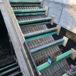 Szczegółowe ujęcie szalunku schodów z widocznym zbrojeniem, drewnianymi elementami konstrukcyjnymi, wiertarką akumulatorową i pudełkiem gwoździ na budowie domu.