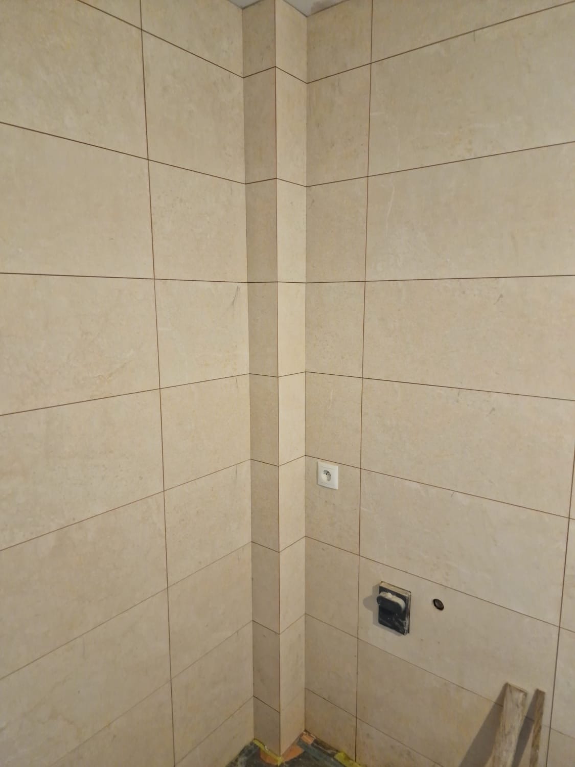 Ściany łazienki w Chorowicach wyłożone beżowymi, poziomymi płytkami ceramicznymi, widoczne gniazdko elektryczne i przygotowane miejsce na armaturę. Na podłodze widoczne fragmenty zabezpieczeń.