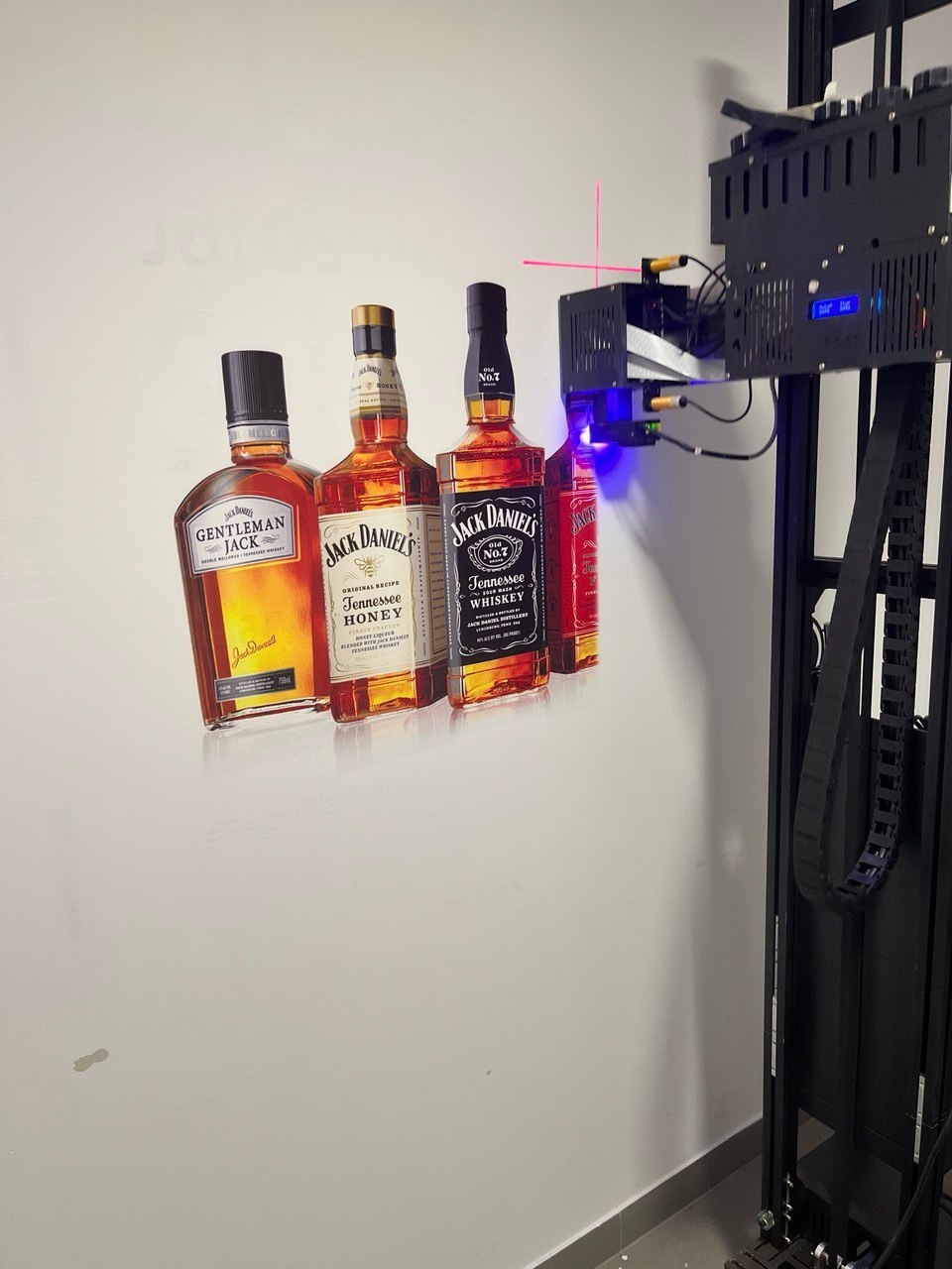Świeżo wydrukowane na ścianie portrety butelek alkoholu, naniesione przez specjalistyczną drukarkę pionową z laserowym pozycjonowaniem.