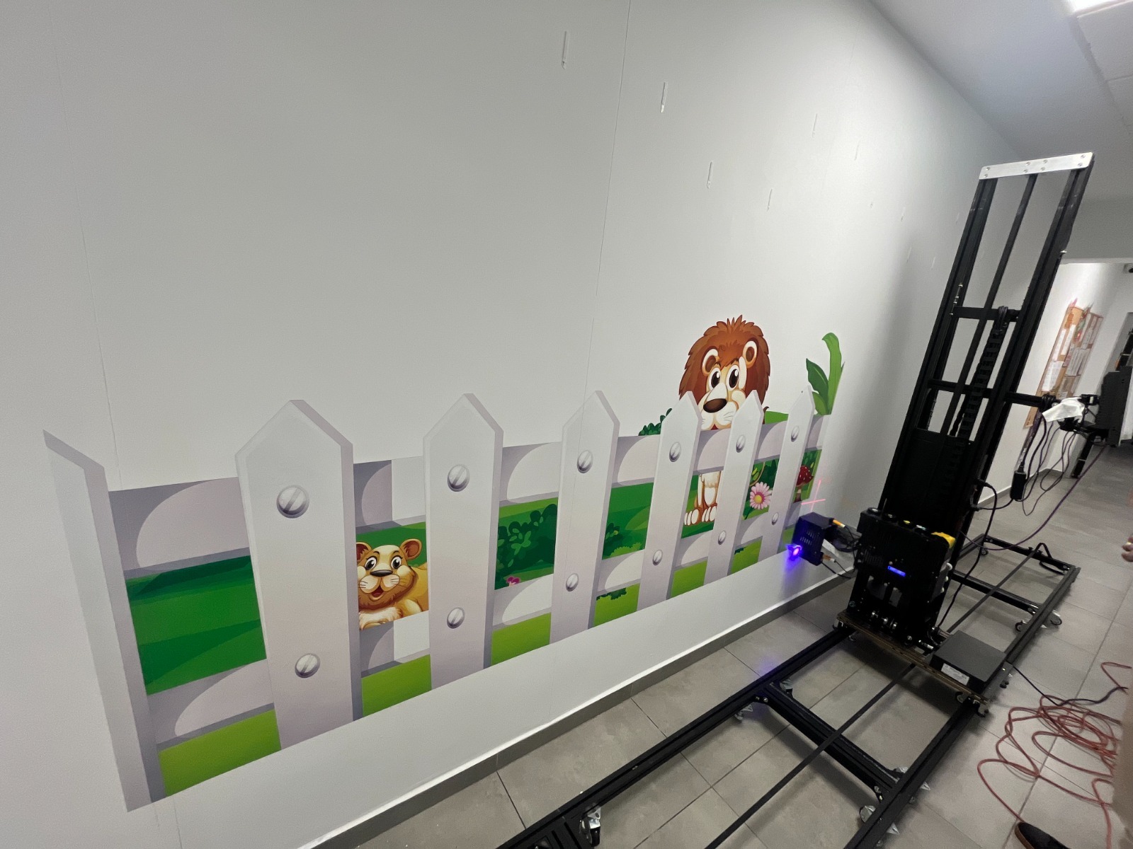 Świeżo nadrukowana grafika z motywem lwa i białego płotu na ścianie, wykonana za pomocą specjalistycznej drukarki mobilnej.