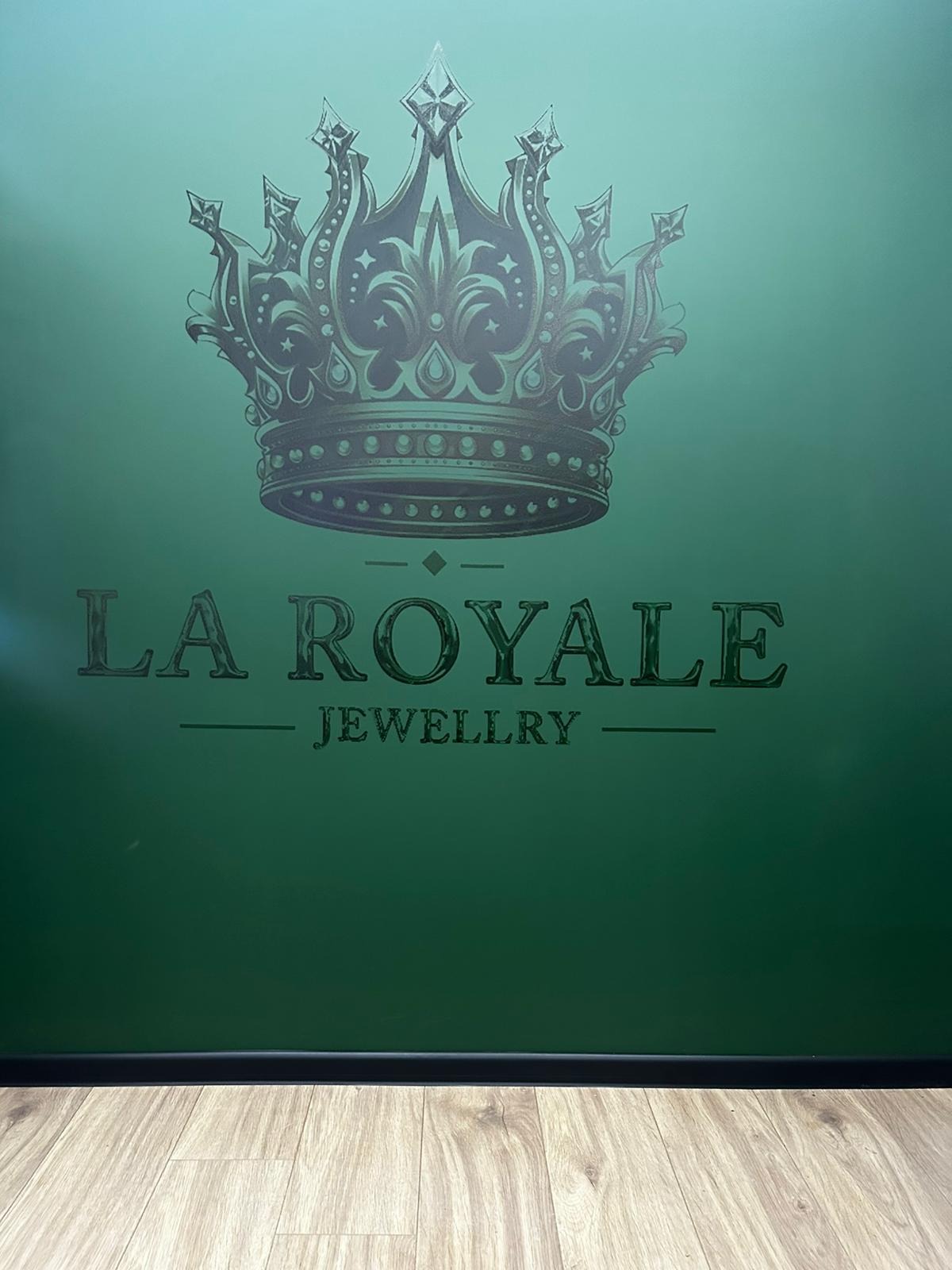 Zielona ściana z ciemnym nadrukiem korony i napisu 'LA ROYALE JEWELLRY', widoczna część podłogi.