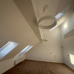 Poddasze po remoncie z drewnianą podłogą, białymi ścianami, oknami dachowymi i nowoczesnymi okrągłymi lampami wiszącymi.
