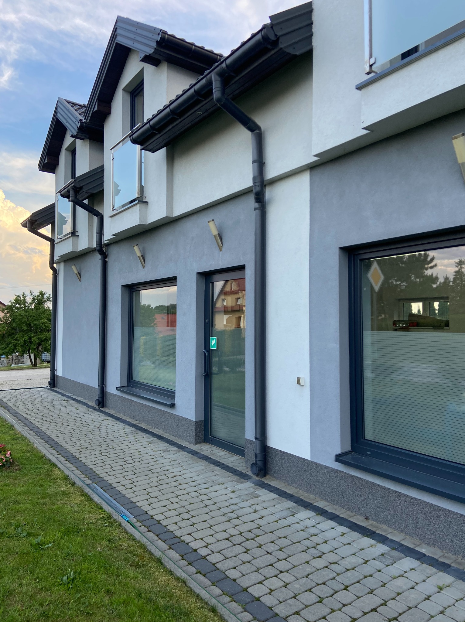 Elewacja budynku z szarymi ramami okiennymi i szklanymi balustradami balkonowymi w Królówce, widok z zewnątrz na chodnik z kostki brukowej.