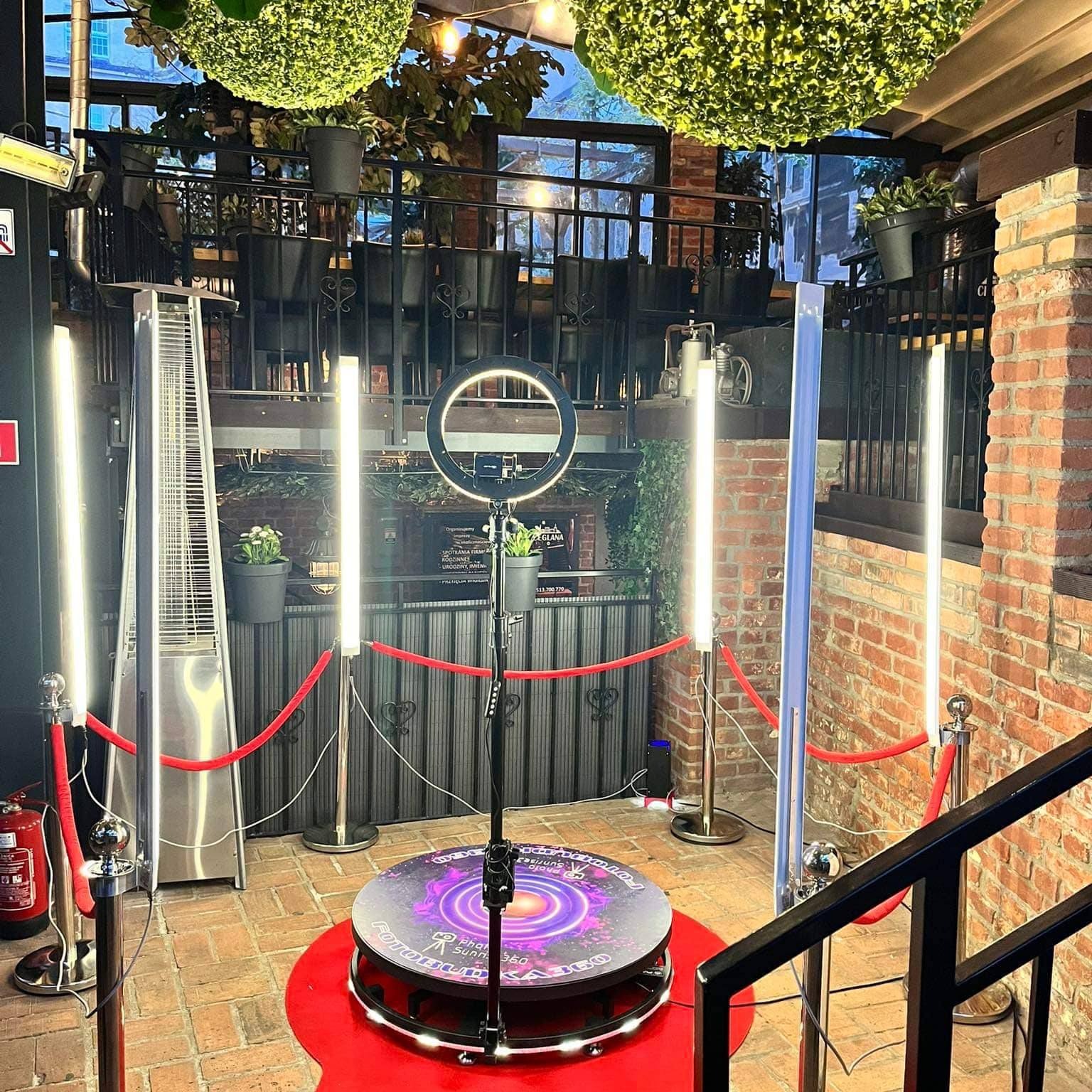 360 stopniowa platforma do nagrywania filmów, otoczona czerwonym dywanem i słupkami z linami, oświetlona lampami pierścieniowymi i listwami LED w Szczecinie, ustawiona w ceglanym wnętrzu...
