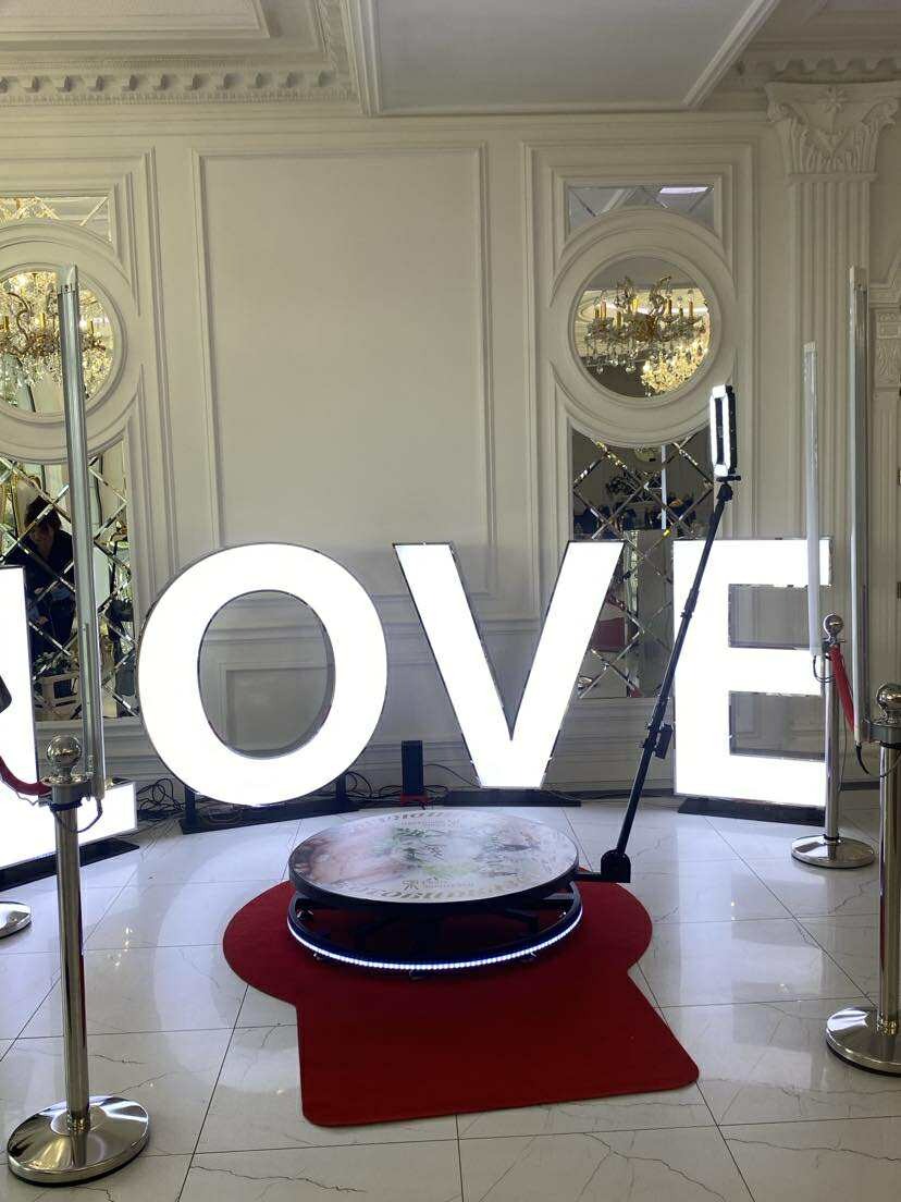 Oświetlona fotobudka 360 z napisem LOVE na czerwonym dywanie. Lustrzane dekoracje ścienne, eleganckie wnętrze. Idealna na wesele lub walentynki.