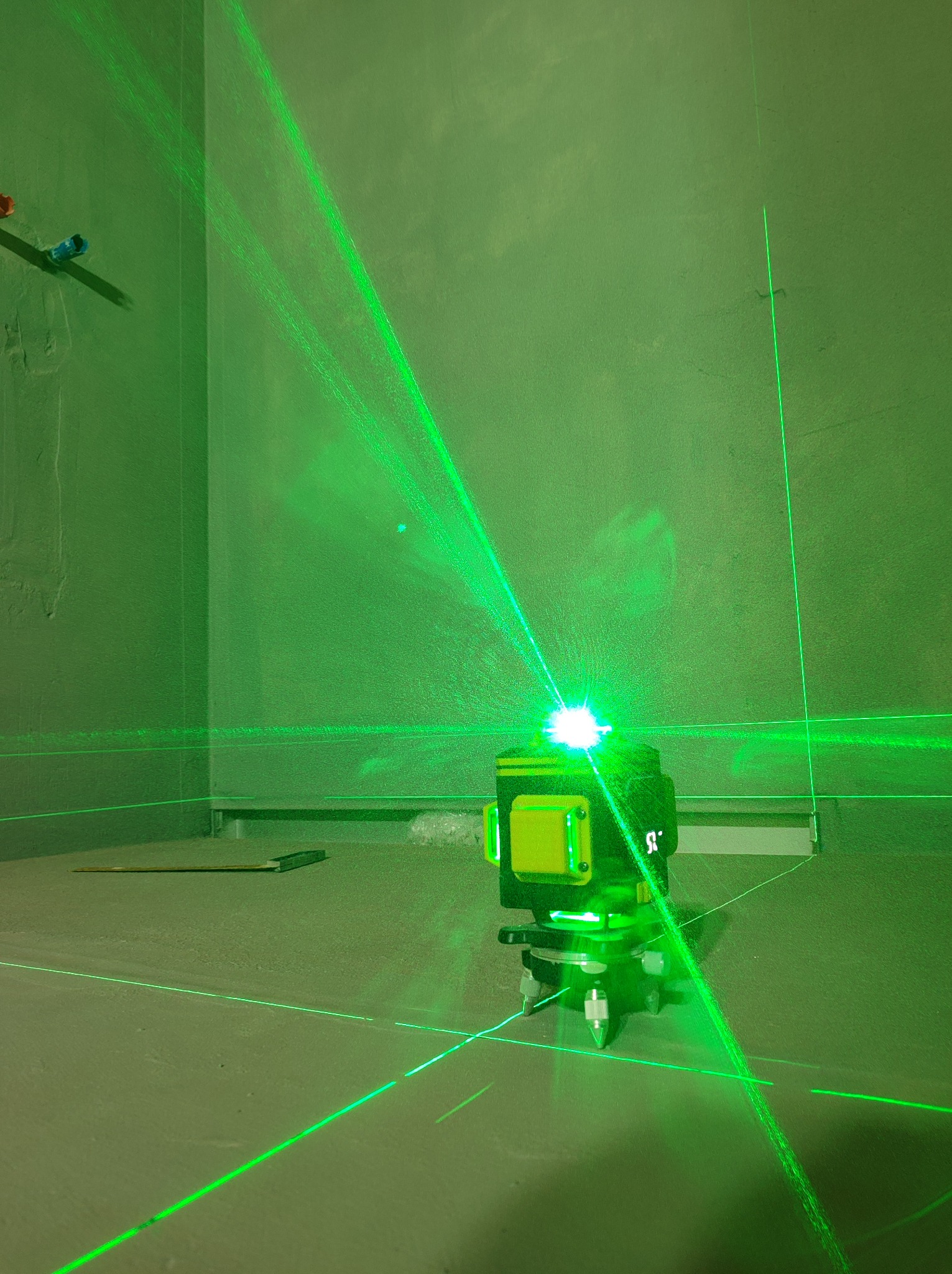 Zielony laser krzyżowy wyznacza poziom na surowych ścianach łazienki w trakcie prac wykończeniowych, widoczne rury instalacyjne.