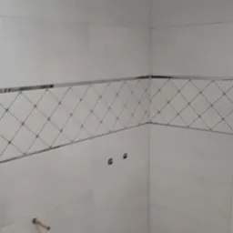 Świeżo wykafelkowana ściana łazienki z dekoracyjnym pasem płytek w romby, widoczne otwory na armaturę i częściowo wykończona podłoga z imitacji drewna.