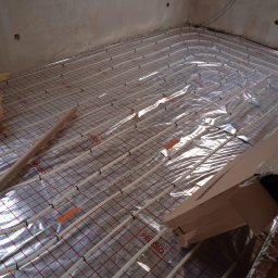 MARBUD MAREK MAJCHERCZYK - Instalacja ogrzewania podłogowego z rurkami na folii z siatką, widok z góry, surowy stan ścian w tle. System PRES.SO.