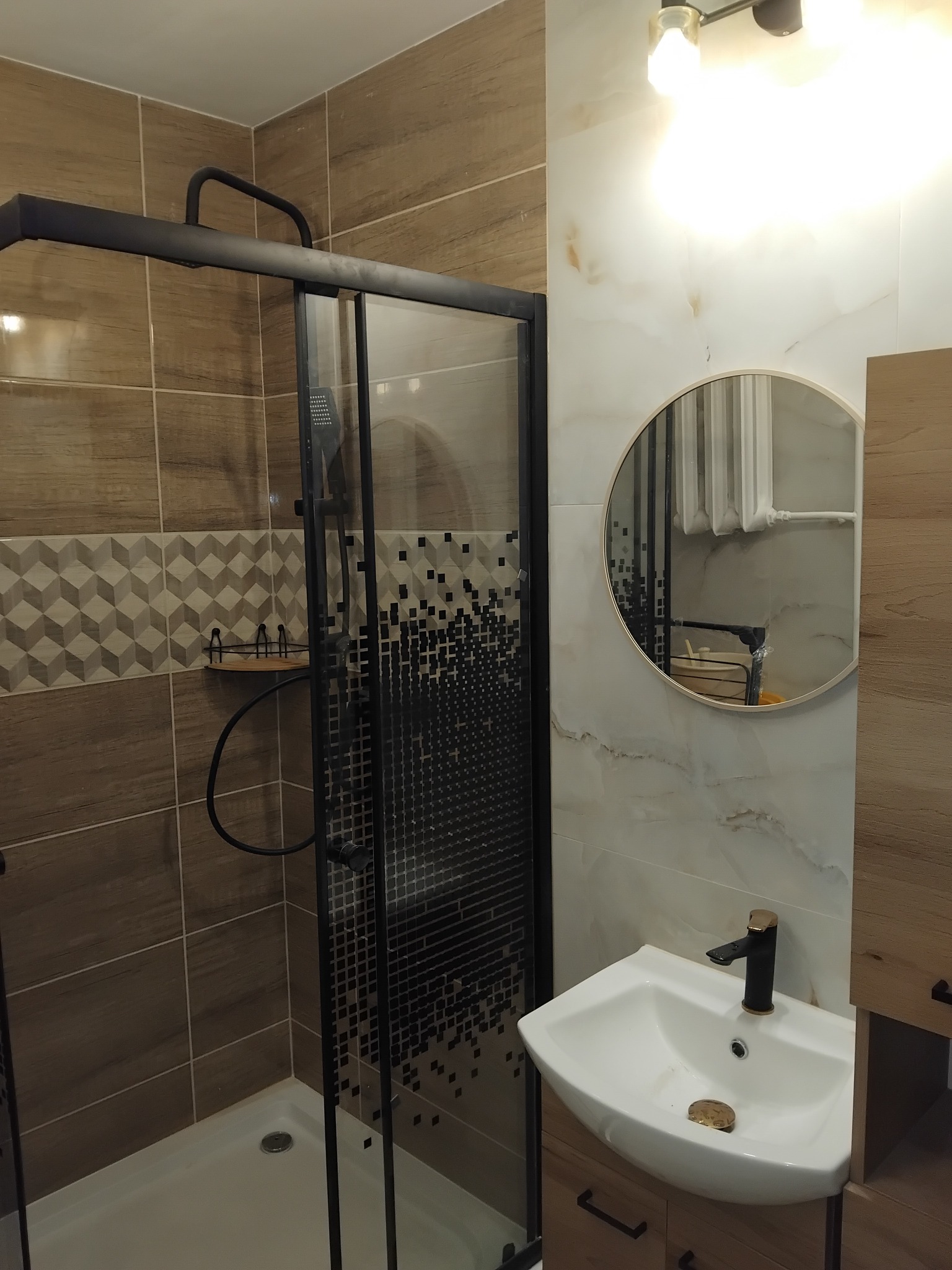 Nowoczesna łazienka z kabiną prysznicową typu walk-in, umywalką nablatową i okrągłym lustrem. Brązowe i białe płytki tworzą elegancki wystrój.