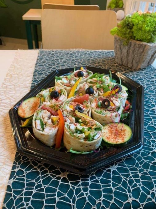 Tortilla wrap rolls filled with chicken, vegetables, and topped with blueberries, arranged on a black octagonal tray with cucumber slices dusted with paprika, placed on a patterned tablecloth.
