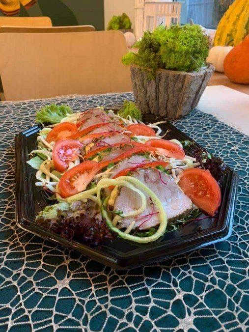 Przystawka z plastrami mięsa, pomidorami i ogórkiem na sałacie, ułożona na czarnym talerzu, z dekoracją z mchu w doniczce w tle.