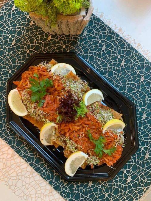 Czerwony ryż z warzywami, kiełkami i cytryną na czarnym, eleganckim talerzu, ułożony na wzorzystej serwetce, z dekoracyjną rośliną w tle.